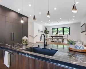 Modern kitchen featuring a black undermount sink with a matching faucet on a black marble island under elegant pendant lighting.