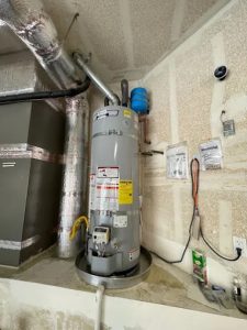 A professional installation of a tall grey gas water heater with an expansion tank and silver venting in a residential utility room.