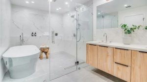 A luxury master bathroom featuring a white freestanding soaking tub, a large glass walk-in shower with marble walls, and a floating wood vanity.