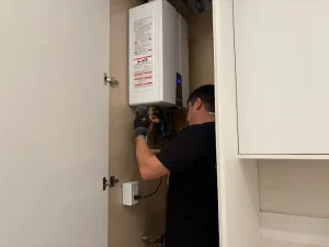 Plumbing technician installing a modern white Navien tankless water heater inside a clean residential utility closet.