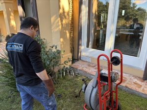 A professional technician using a motorized drain snake machine to clear a residential sewer line on an outdoor patio.