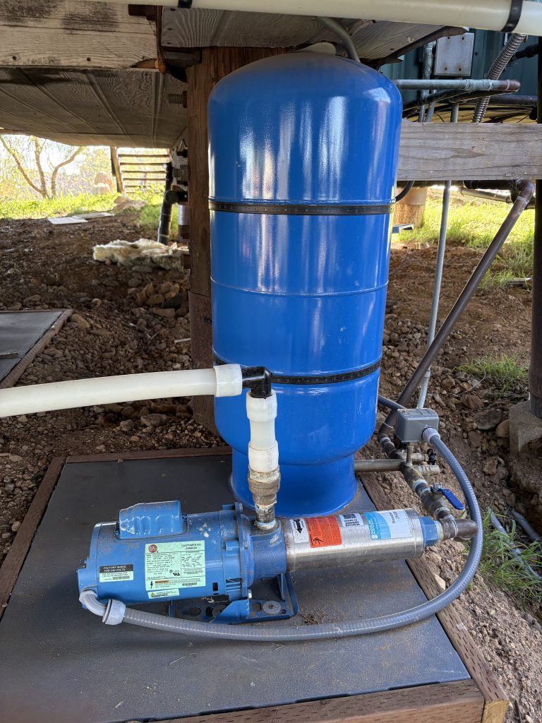 A professional installation of a blue well pressure tank and a horizontal water pump motor on a protective outdoor pad.