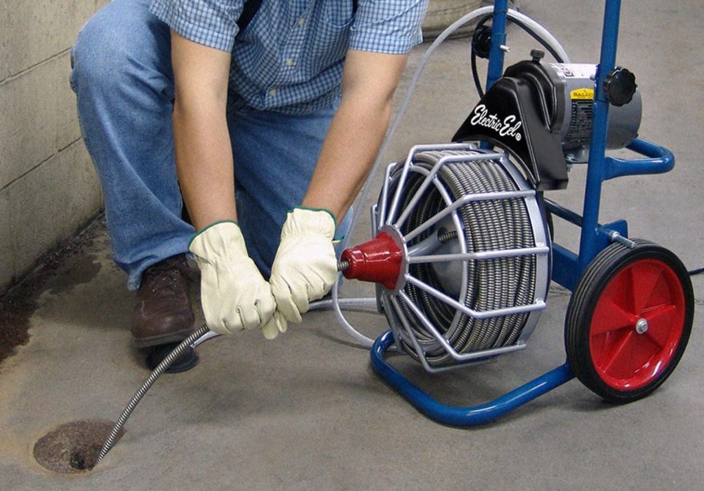Technician using an Electric Eel drain cleaning machine to clear a stubborn blockage in a floor drain.