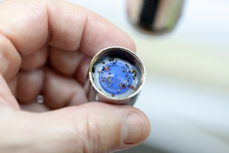 Hand holding a chrome faucet aerator filled with dark sediment and mineral debris from a clogged water line.