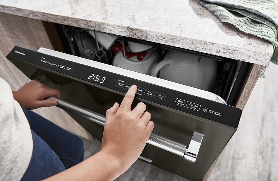 A person selecting wash cycles on a modern KitchenAid dishwasher control panel with a granite countertop.