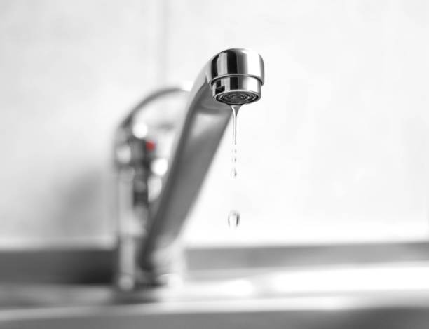 Close up of a leaky chrome kitchen faucet with water droplets dripping into a sink.
