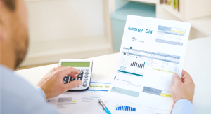 Over the shoulder shot of a man reading his energy bill in his right hand with his left hand over a calculator.
