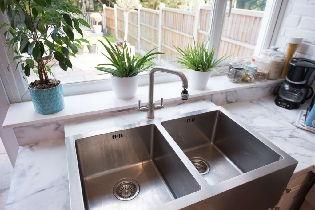 A clean double bowl stainless steel farmhouse kitchen sink with a modern faucet installed on a marble countertop.