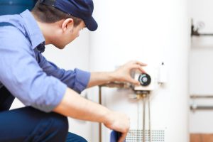 Man in a blue uniform and blue hat adjusting the temperature on a pilot for a tank water heater