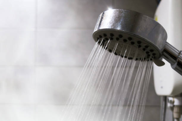Hot water coming out of a shower head in a steamy bathroom.