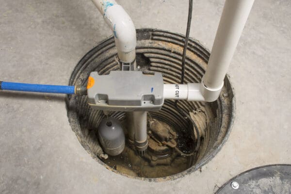 Sump pump pit located in the basement with drainage pipes coming out of the pit.