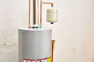 Tank water heater with a flexible water supply line and a expansion tank with a white wall behind it.