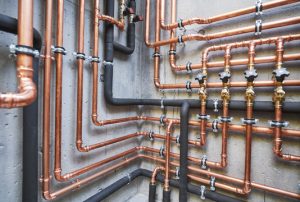 Intricate network of professional copper plumbing lines and insulated pipes with multiple shutoff valves mounted on a concrete wall.