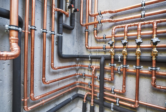 Intricate network of professional copper plumbing lines and insulated pipes with multiple shutoff valves mounted on a concrete wall.
