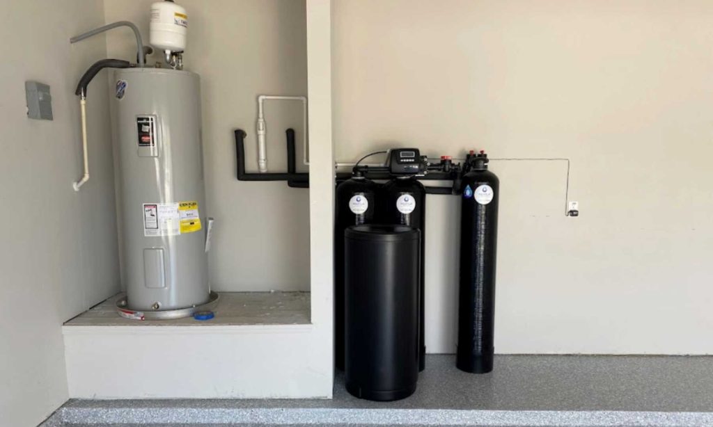 Residential garage installation featuring a tall grey hot water heater next to a multi tank black water softener and filtration system.